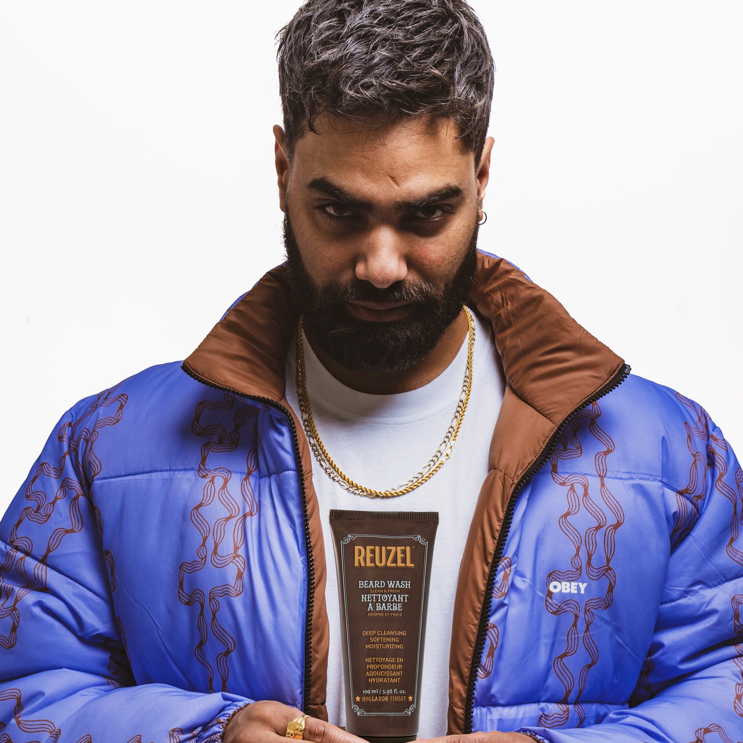Male model with short black hair and beard holding REUZEL beard wash