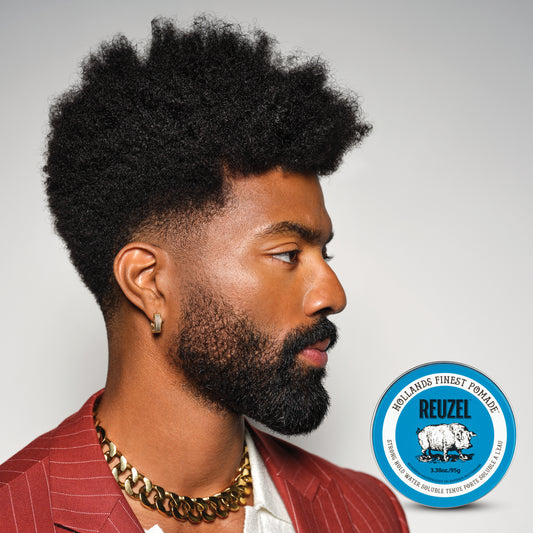 Man with highly textured hair and a beard, hair styled with Reuzel Blue Strong Hold Water Soluble Pomade, wearing a red jacket, with Reuzel logo in the corner.