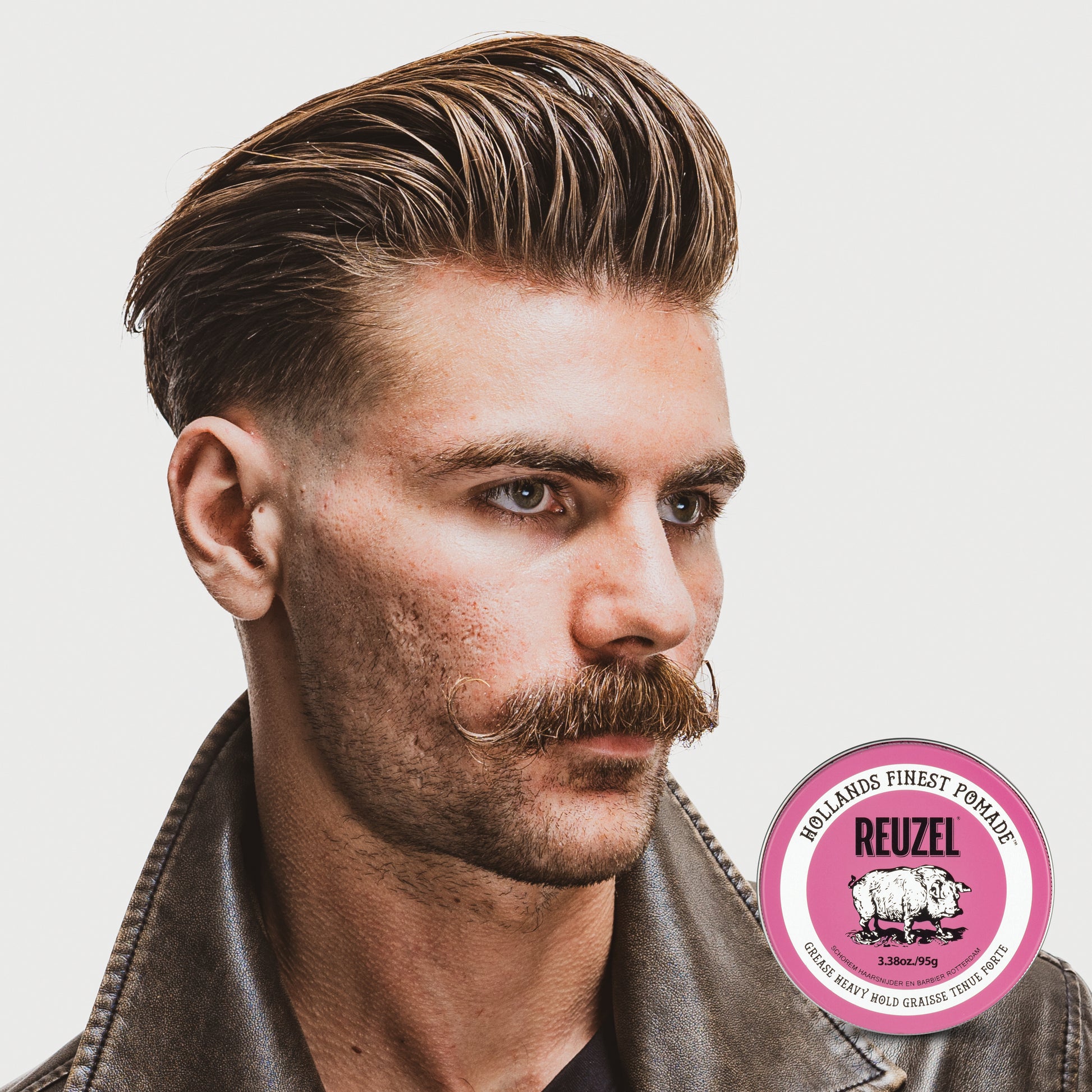 Man with slicked back hair and mustache, hair styled with Reuzel Pink Grease Heavy Hold Pomade, wearing a leather jacket, with Reuzel logo in the corner.