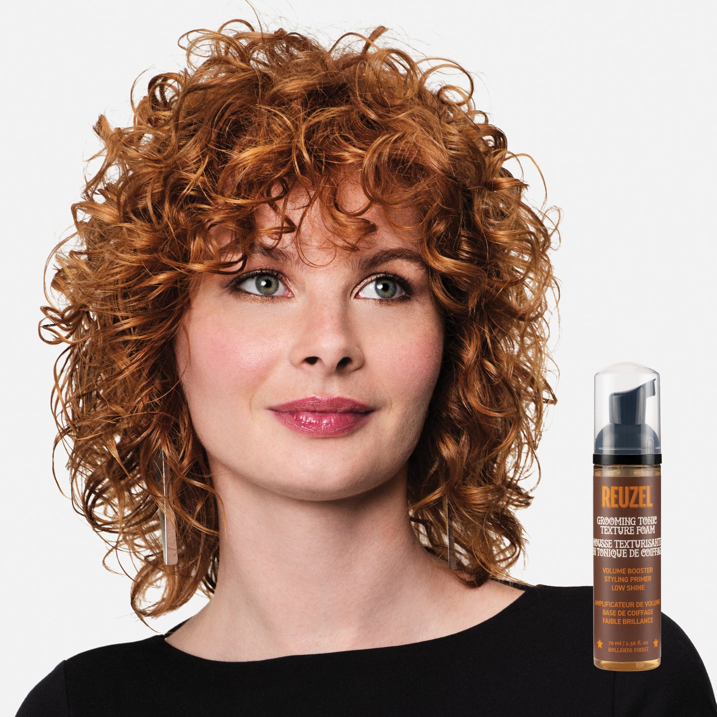 Woman with curly hair next to a bottle of ReuzelGrooming Tonic Texture Foam