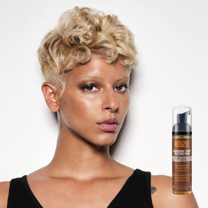Woman with styled hair next to a bottle of Reuzel Grooming Tonic Texture Foam